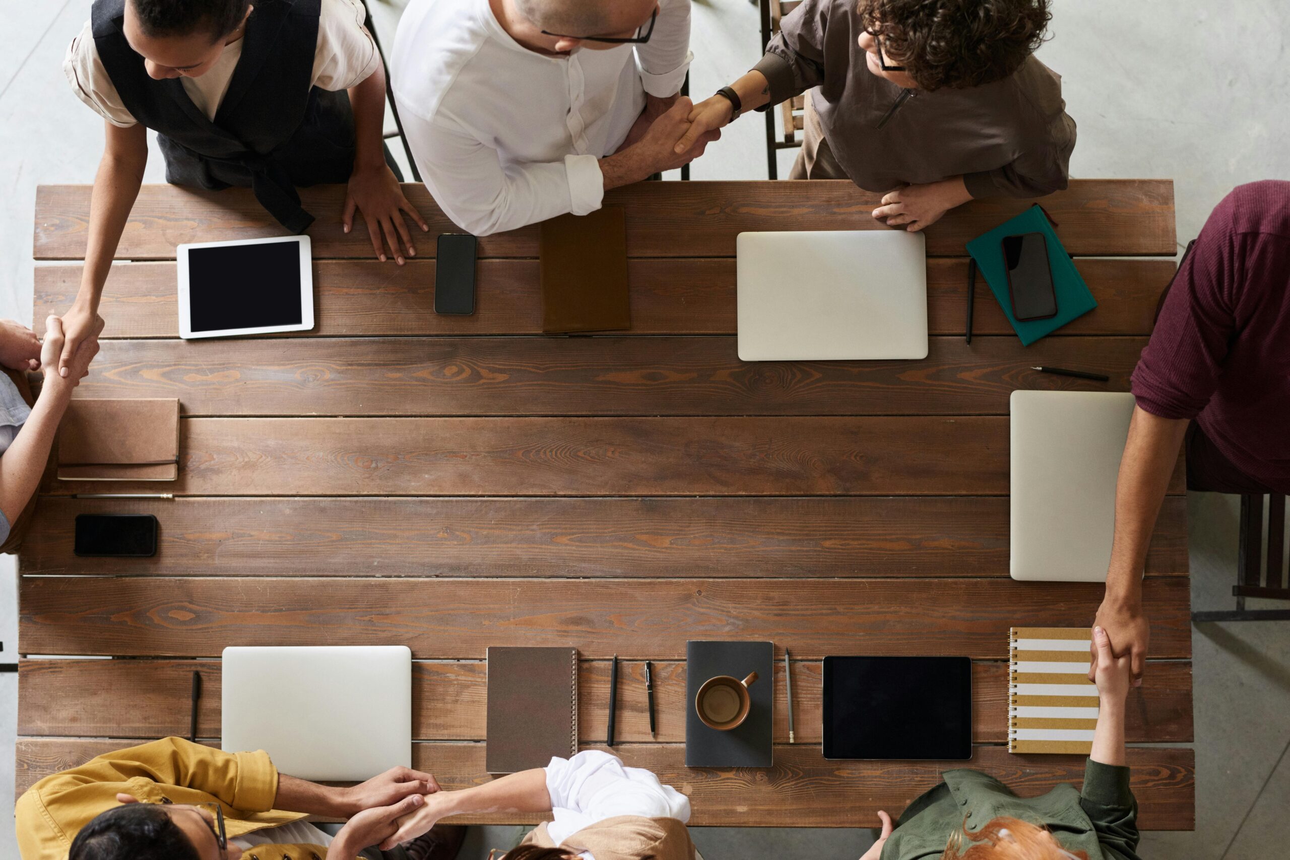 Group of adults having a business meeting, discussing plans around a wooden table with tech devices.