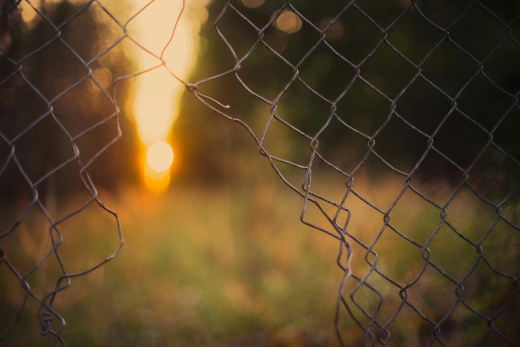 A sunset seen through a cyclone fence with a bokeh effect, highlighting nature's beauty.