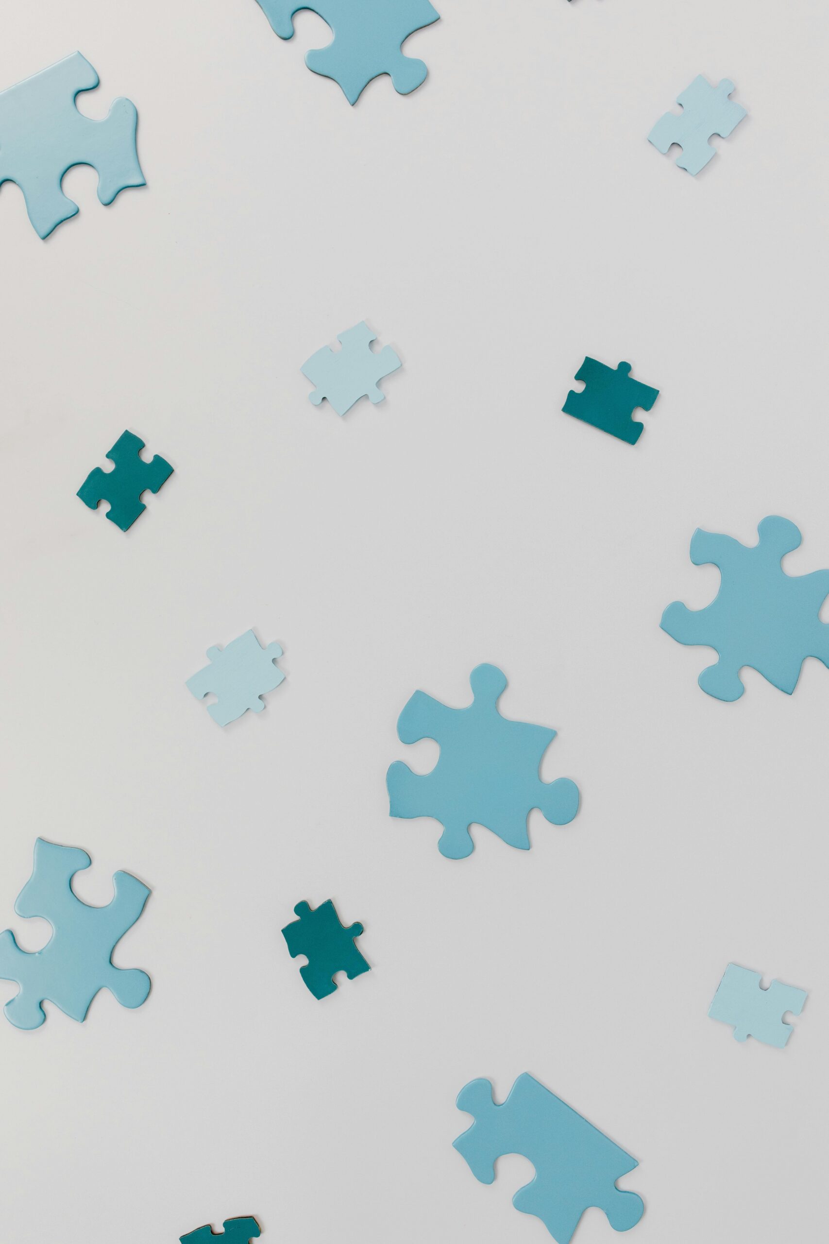 Close-up of varied blue puzzle pieces scattered randomly on a white surface.