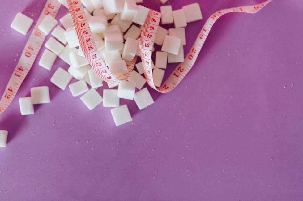White sugar cubes with a pink tape measure on a purple surface, symbolizing diet awareness.